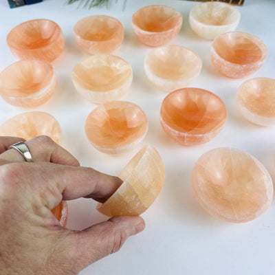 Orange Selenite Bowls on a table, with one in a hand showing side view