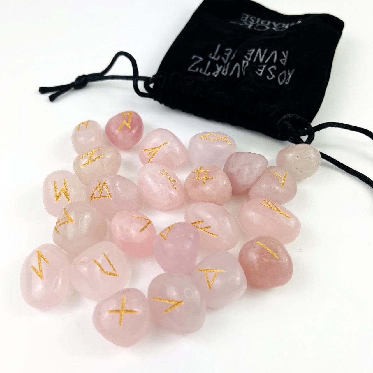 rose quartz tumbled stones with the rune alphabet engraved in gold , spilling out of a black velvet bag