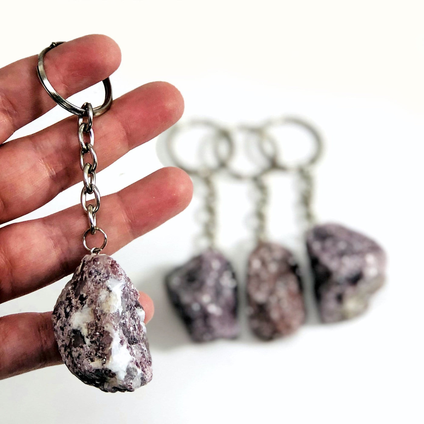 hand holding up lepidolite keychain with others in the background