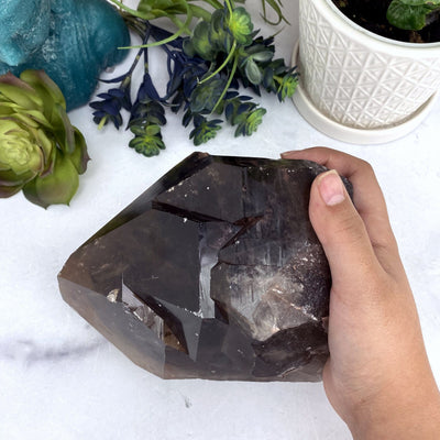 hand holding up Large Alligator Smoky Quartz with decorations in the background