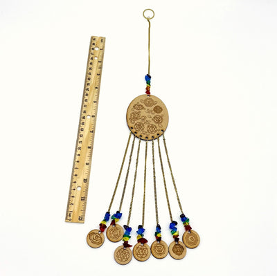 Engraved Wooden 7 Chakras hanging next to a ruler on white background.
