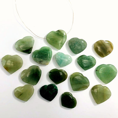 multiple green aventurine head drilled heart shaped gemstones in a row one with a wire shown as a neckless
