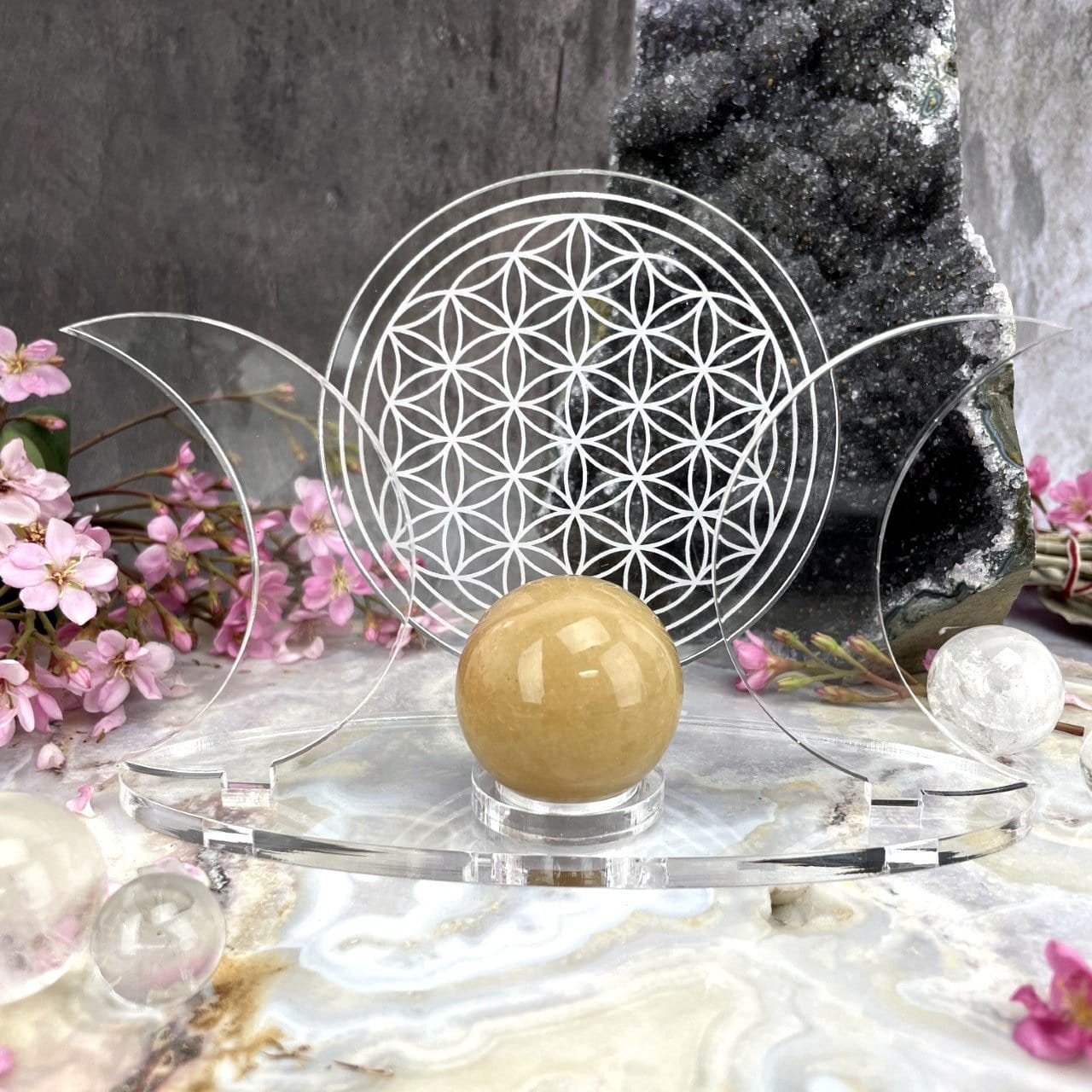 Acrylic Sphere Holder Crescent Moons - Flower of Life holding a sphere in an alter that consists of crystals and flowers.