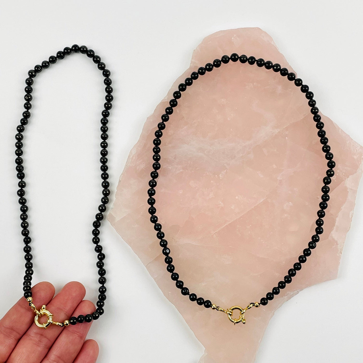 hand holding Shungite Candy Necklace with another on a rose quartz platter