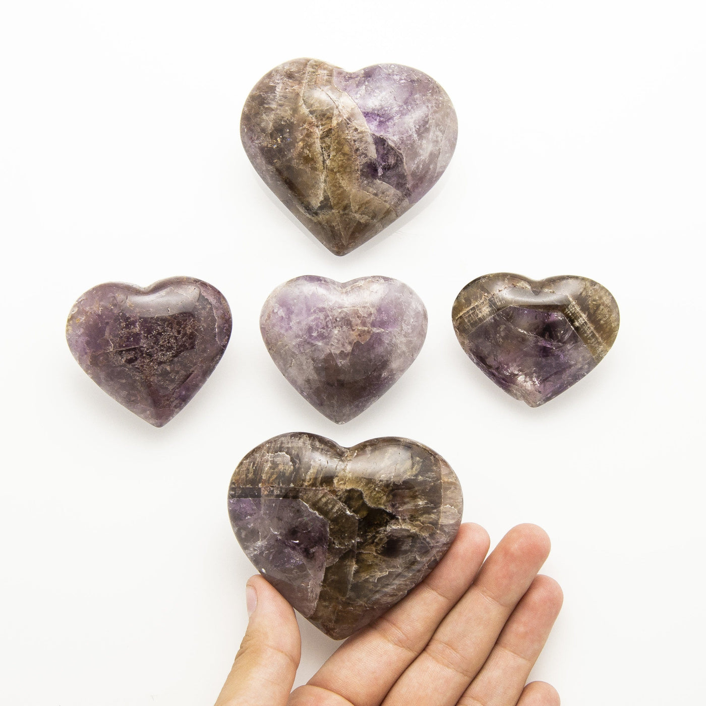 two different sizes of seven mineral stone heart with a hand to show size reference