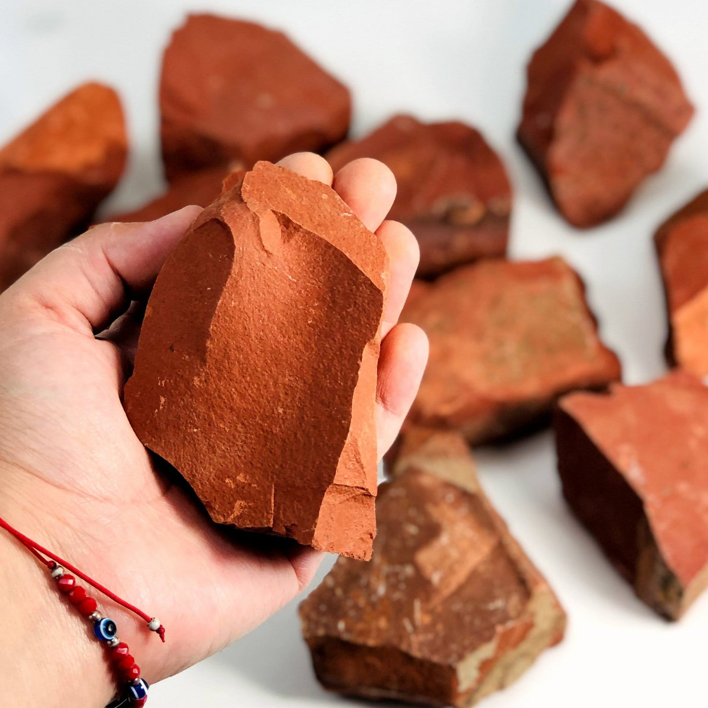 Hand holding up Red Jasper Rough Stone with others blurred in the background