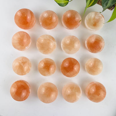 16 orange selenite bowls on a table showing color variations, shown from overhead'