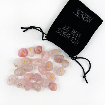 rose quartz tumbled stones with the rune alphabet engraved in gold , spilling out of a black velvet bag