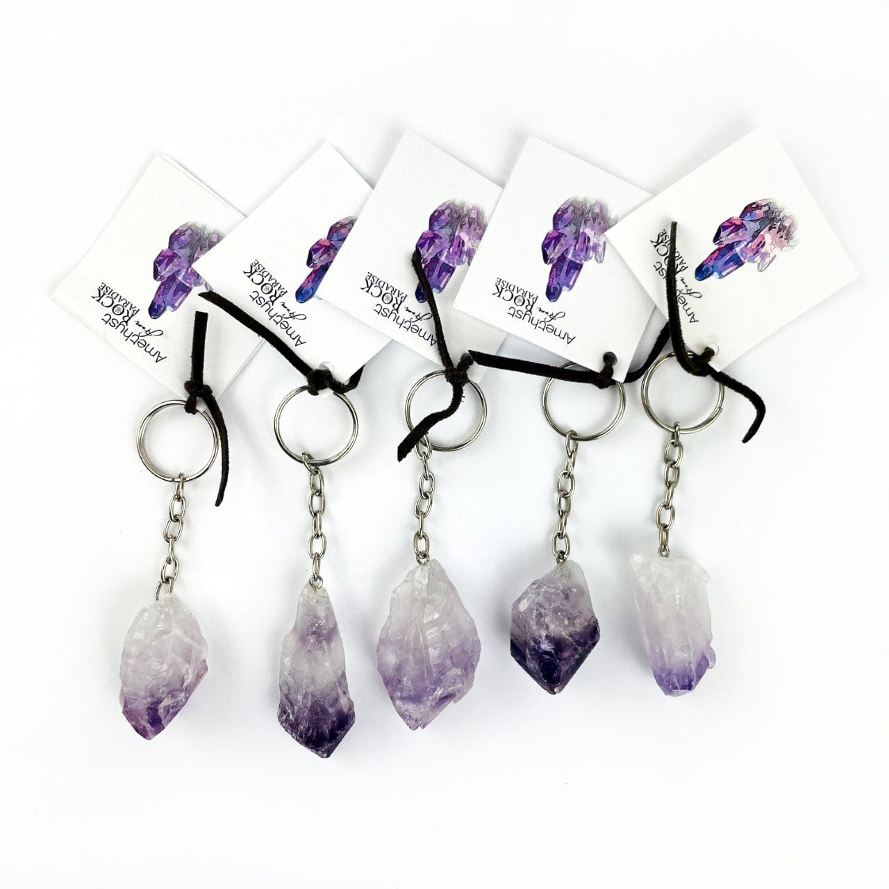 5 Amethyst Keychains with tags on a table showing size and shape variations of this stock.