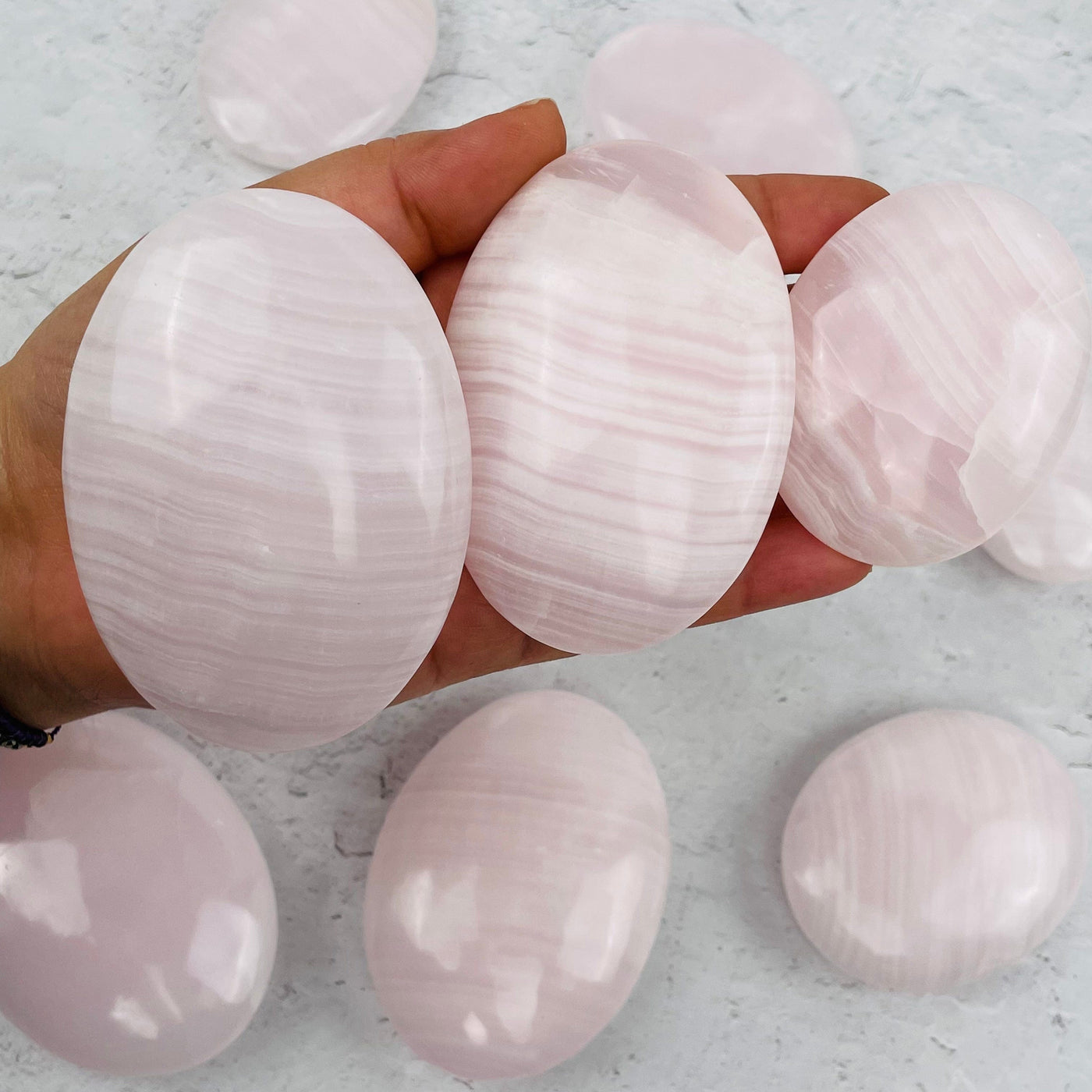 multiple Mangano Calcite Palm Stones in hand for size reference 