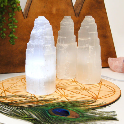 selenite raw crystal tower light turned on in natural light with others in background display