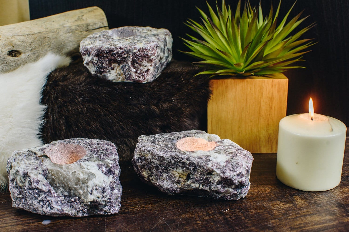 3 lepidolite stone candle holders with a candle burning next to them on a wood background