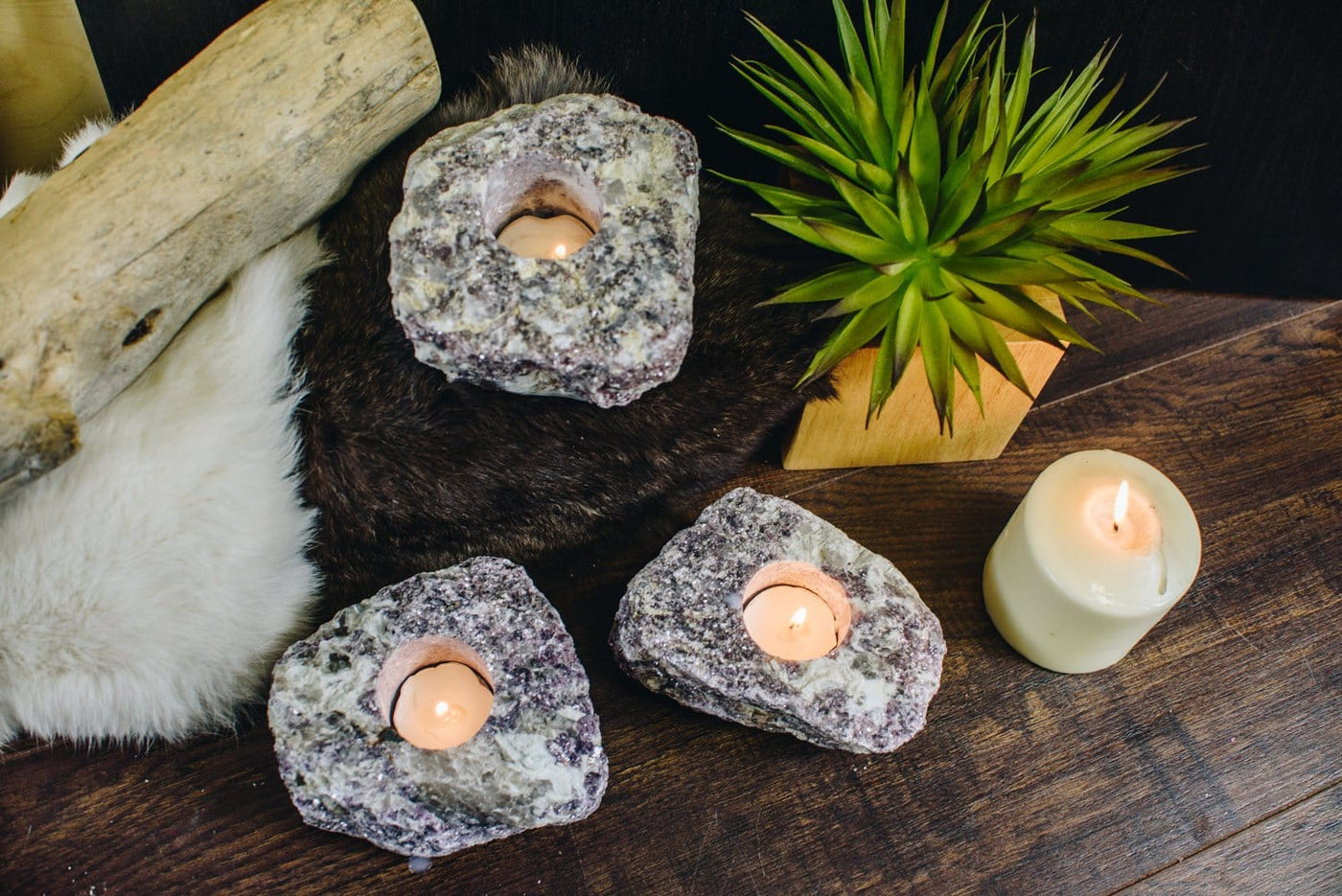 top view of 3 lepidolite stone candle holders with candles burning inside of them on a wood background