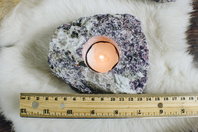 one lepidolite candle holder with a candle burning in it on a piece of white fur next to a ruler