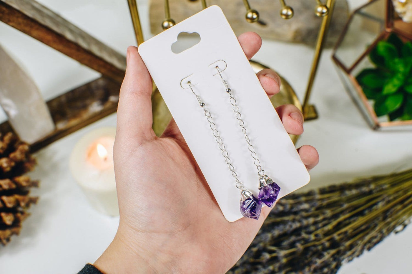 Amethyst point earrings in silver plated on a white hang card and held in a woman's hand.