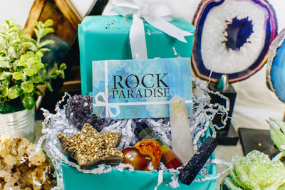 A blue card with Rock Paradise written on it surrounded by assorted crystals.