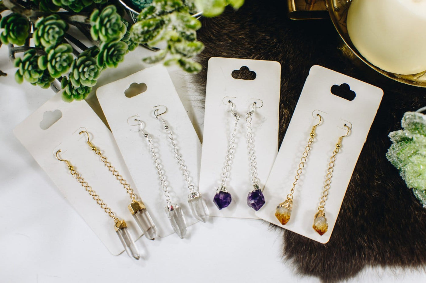 4 pairs of earring on white hang cards.  Each has crystals hanging from a chain that is approximately 2 inches long.  Pictured in order is crystal quartz point in gold, crystal quartz point in silver, amethyst points in silver, and citrine in gold.