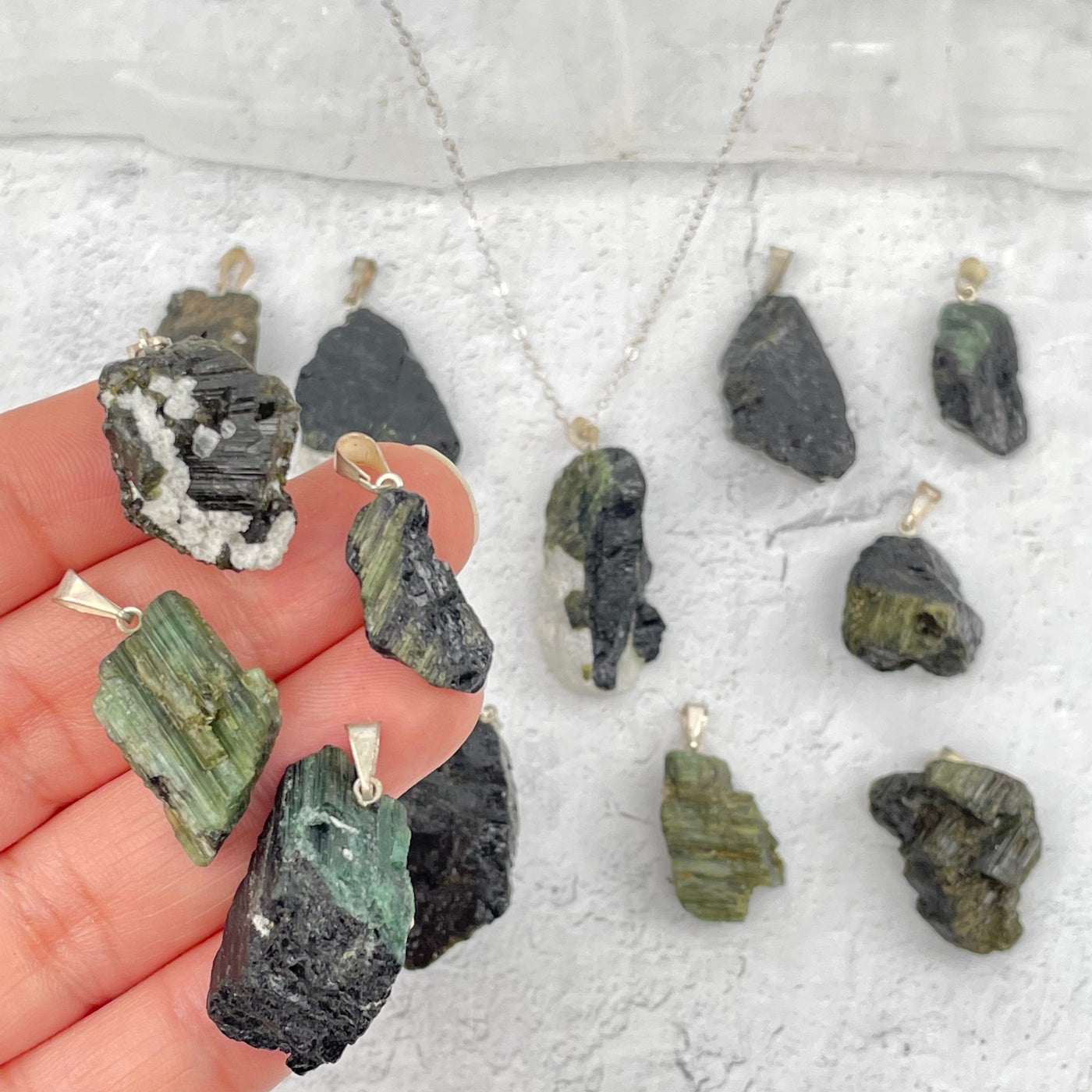 multiple green tourmaline pendants in hand for size reference 