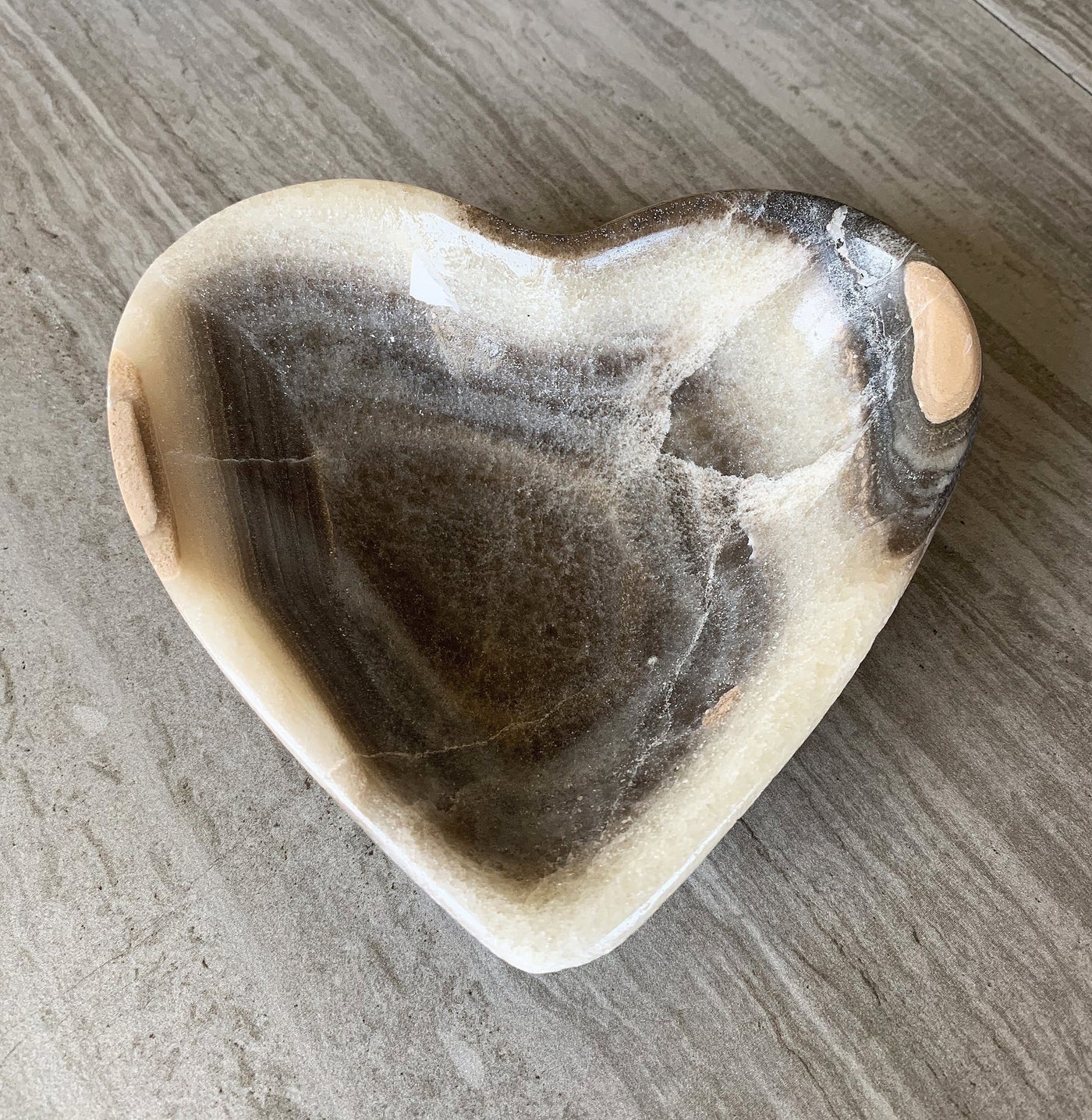 Mexican onyx heart bowl in shades of brown, tan and cream on a wood background.
