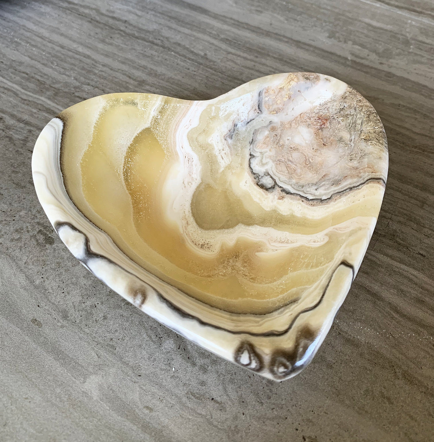 mexican onyx bowl in shades of yellow, white, cream, tan and black on a wood background.