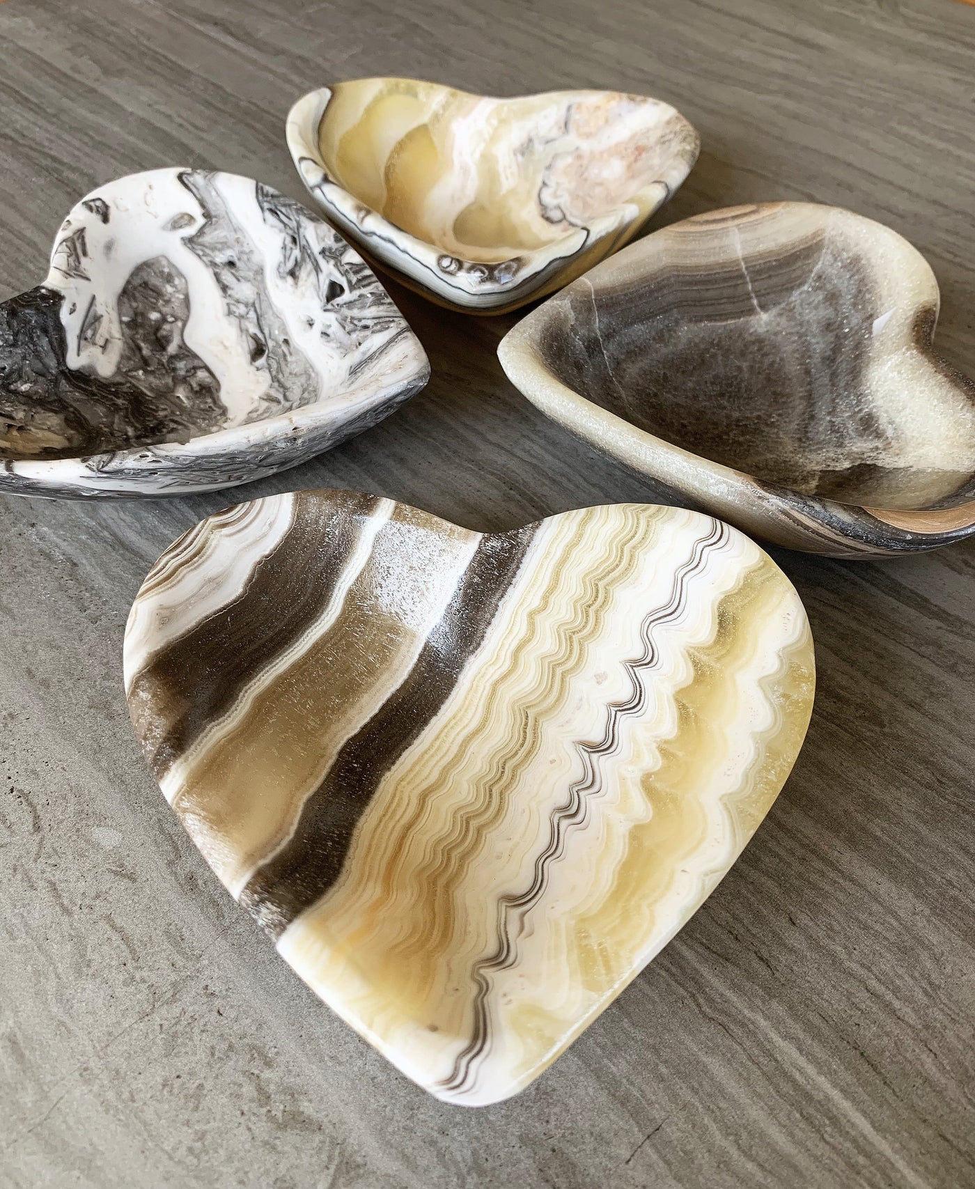 assortment of mexican onyx heart bowls shown to display they vary in color and patterns with shades of white, yellow, tan, cream, and black.