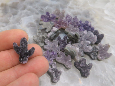 Multiple amethyst cactus being are being displayed on a crystal quartz platter, one is being held for size reference. 