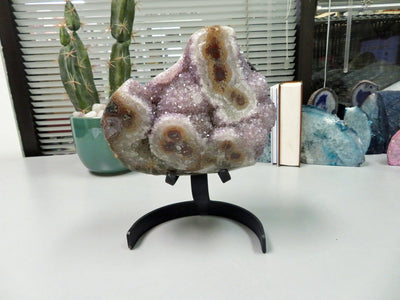 amethyst formation with stalactites on metal stand with decorations in the background