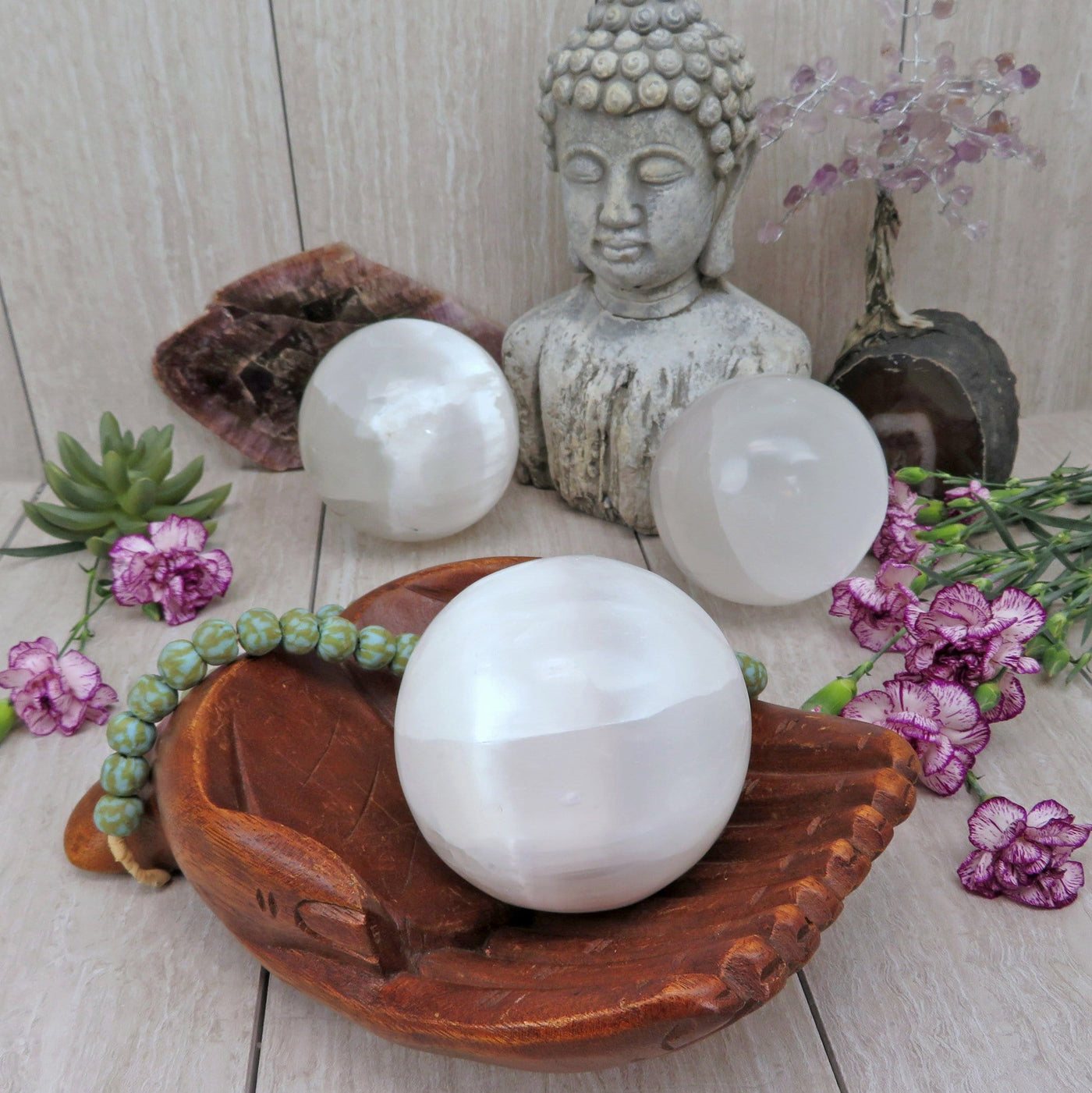selenite sphere in wooden hand bowl with others in background display