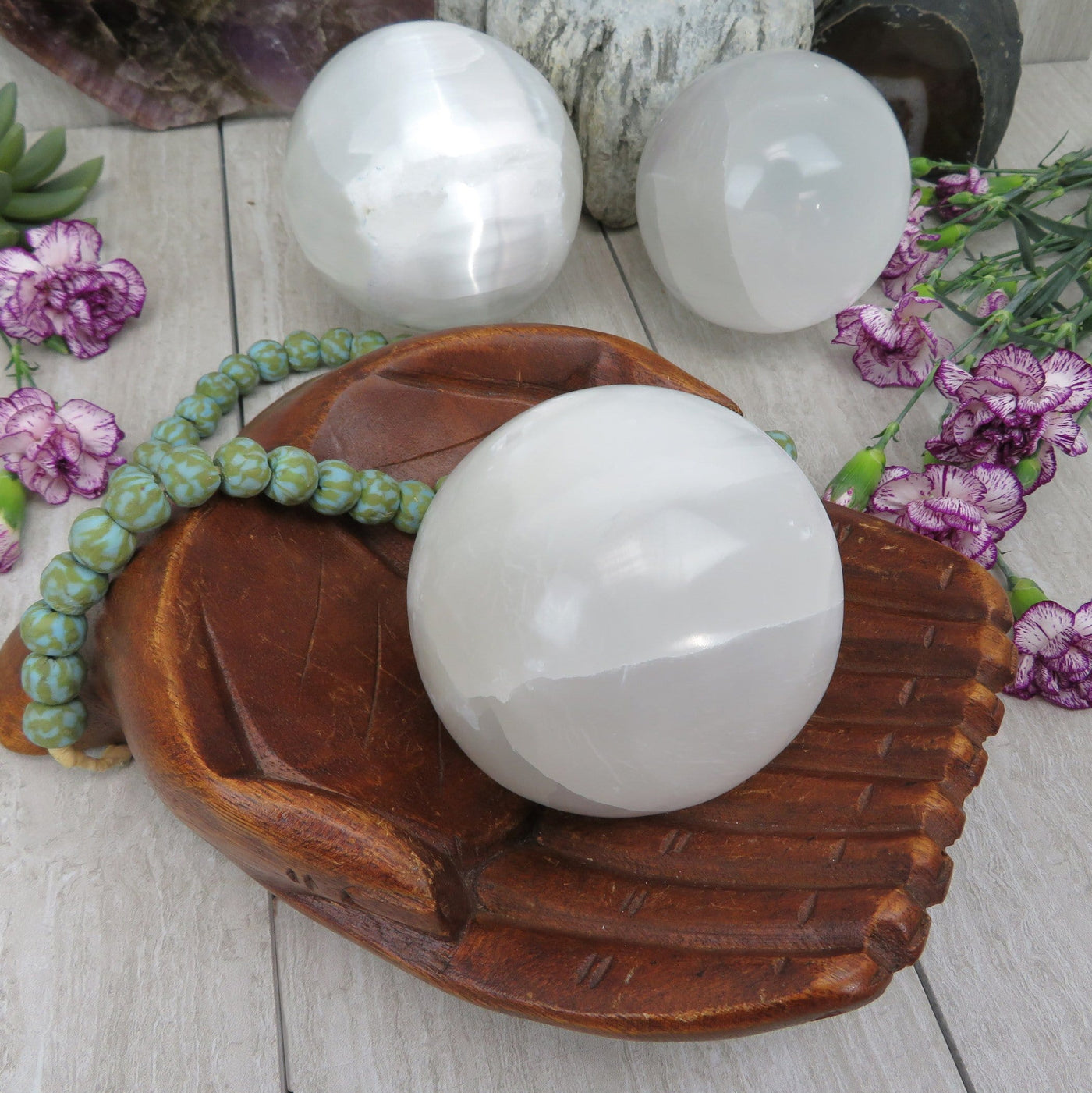 selenite sphere in wooden hand bowl with others in background display