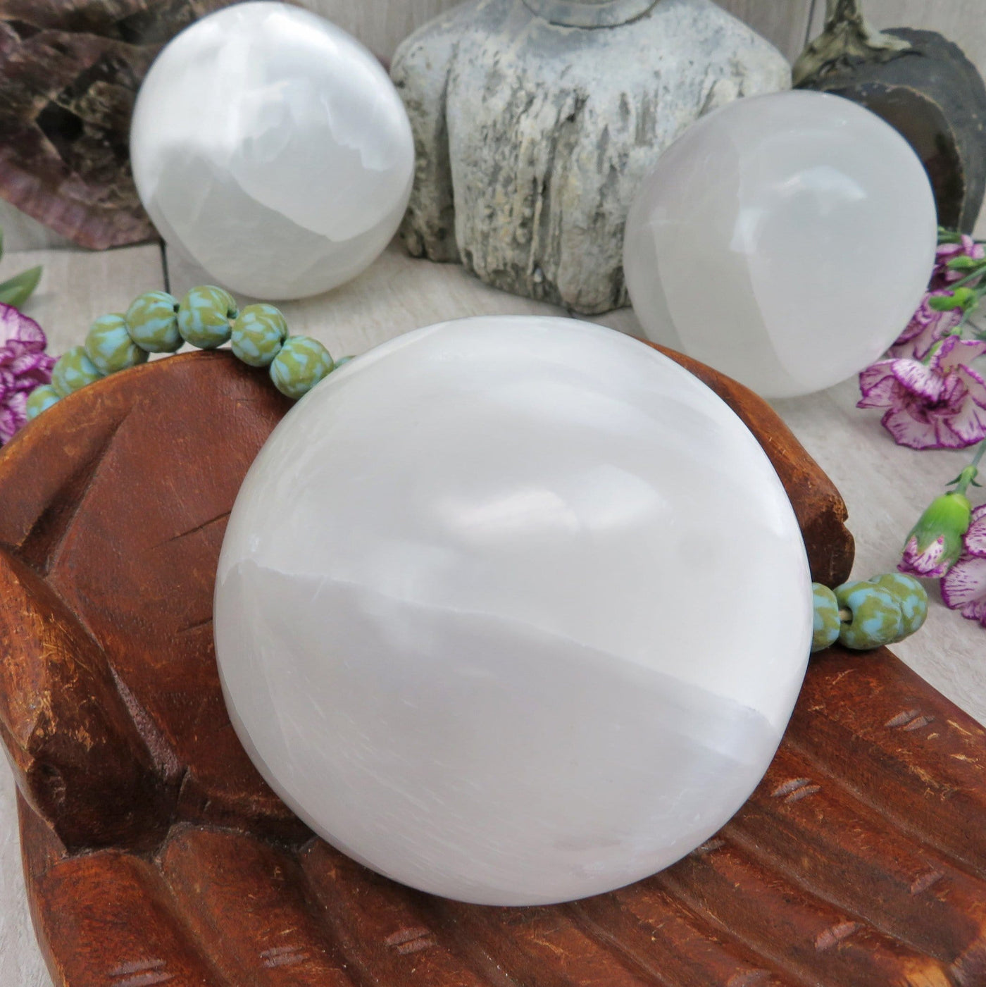 close up of selenite sphere in wooden hand bowl for details with others in background display