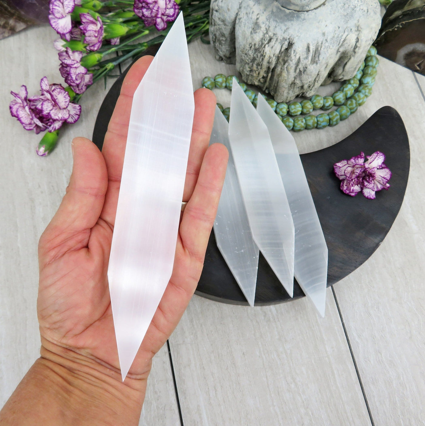 hand holding up Selenite Flat Double Point with others in the background with decorations