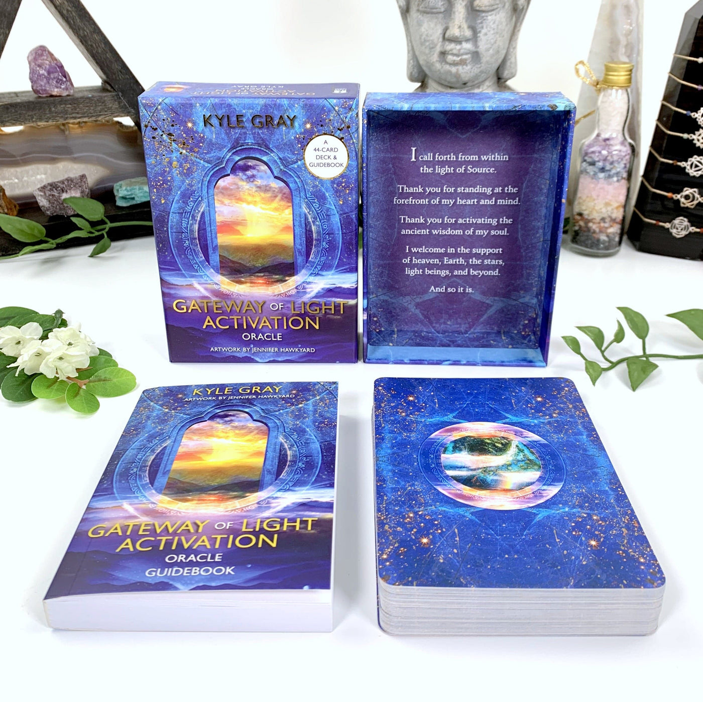 Image of contents of the box on a white background with a budha and some crystal props behind it.  Image shows box comes with a guidebook. Cards are blue with stars on them and a circle showing an outdoor sunset