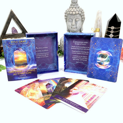 another image on white background showing the contents of the oracle box.  Box is blue with a window showing a sunset.  Pictured is the oracle guide book and some cards from the deck.