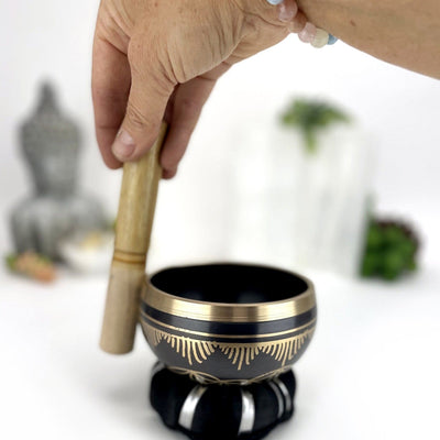 Brass Singing Bowl Set in Black Color with Gold showing a person demonstrating with a wood pallet