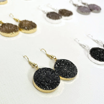 close up of black titanium treated druzy earrings in gold plate with other druzy earrings on a white background
