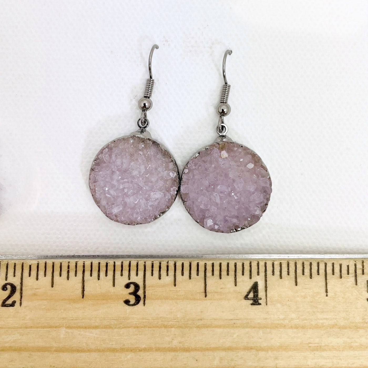 White druzy earrings on a white background next to a wooden ruler.  Each earring is approximately 3 fourths of an inch in diameter.