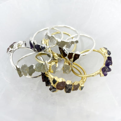 Pile of Raw Stone Rings in gold and silver on stone background