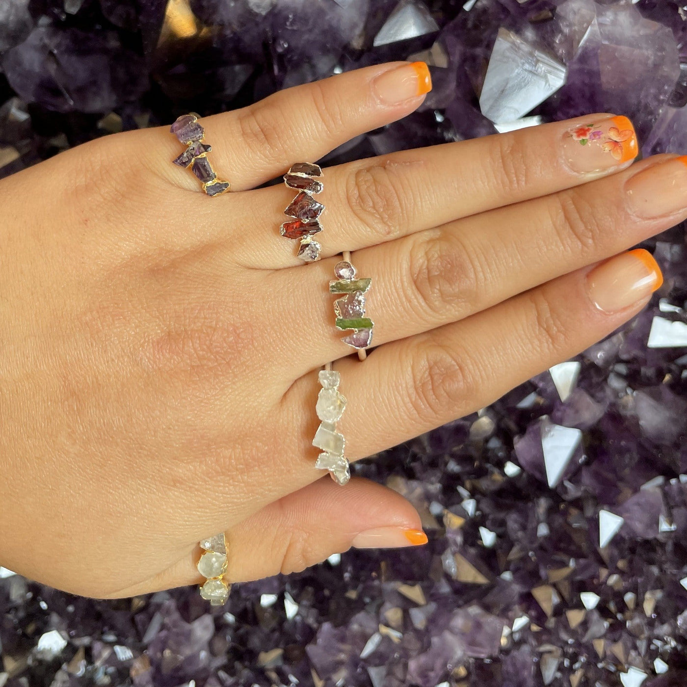 Hand wearing 5 Raw Stone Rings with amethyst background