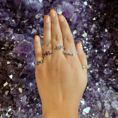 Hand wearing 5 Raw Stone Rings on amethyst background
