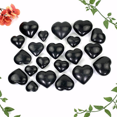 A multitude of polished black onyx hearts on a white background with vines and floras decorating the background