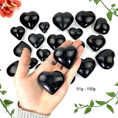 2 - 51 gram to 100 gram black onyx polished hearts on a hand in front of the opening shot 