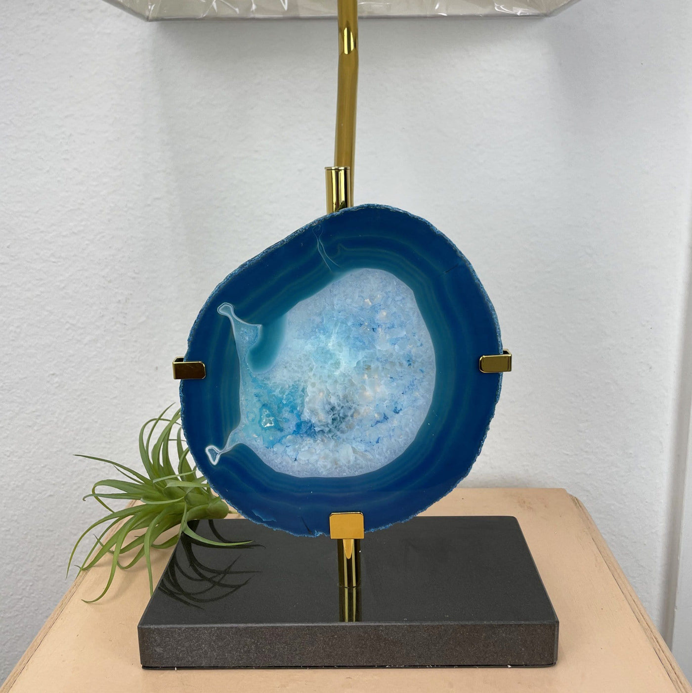 A teal agate slice on a gold lamp on top of a table