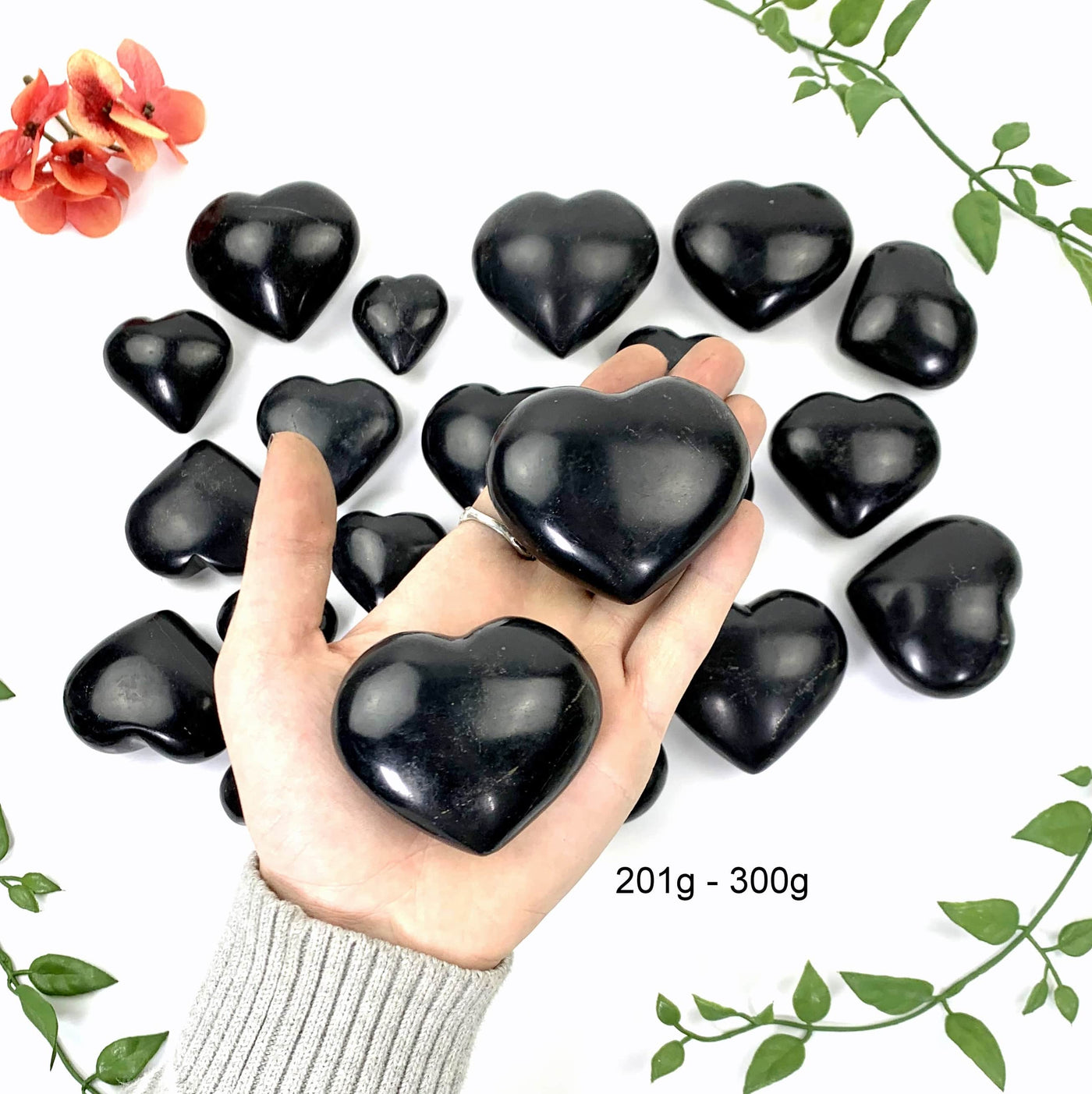 2 - 201gram to 300gram black onyx polished hearts on hand in front of opening shot