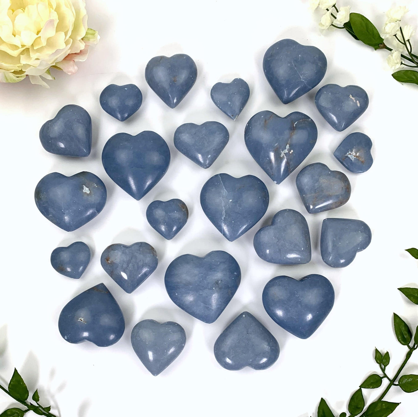 a multitude of light blue angelite hearts on a white background surrounded by flowers