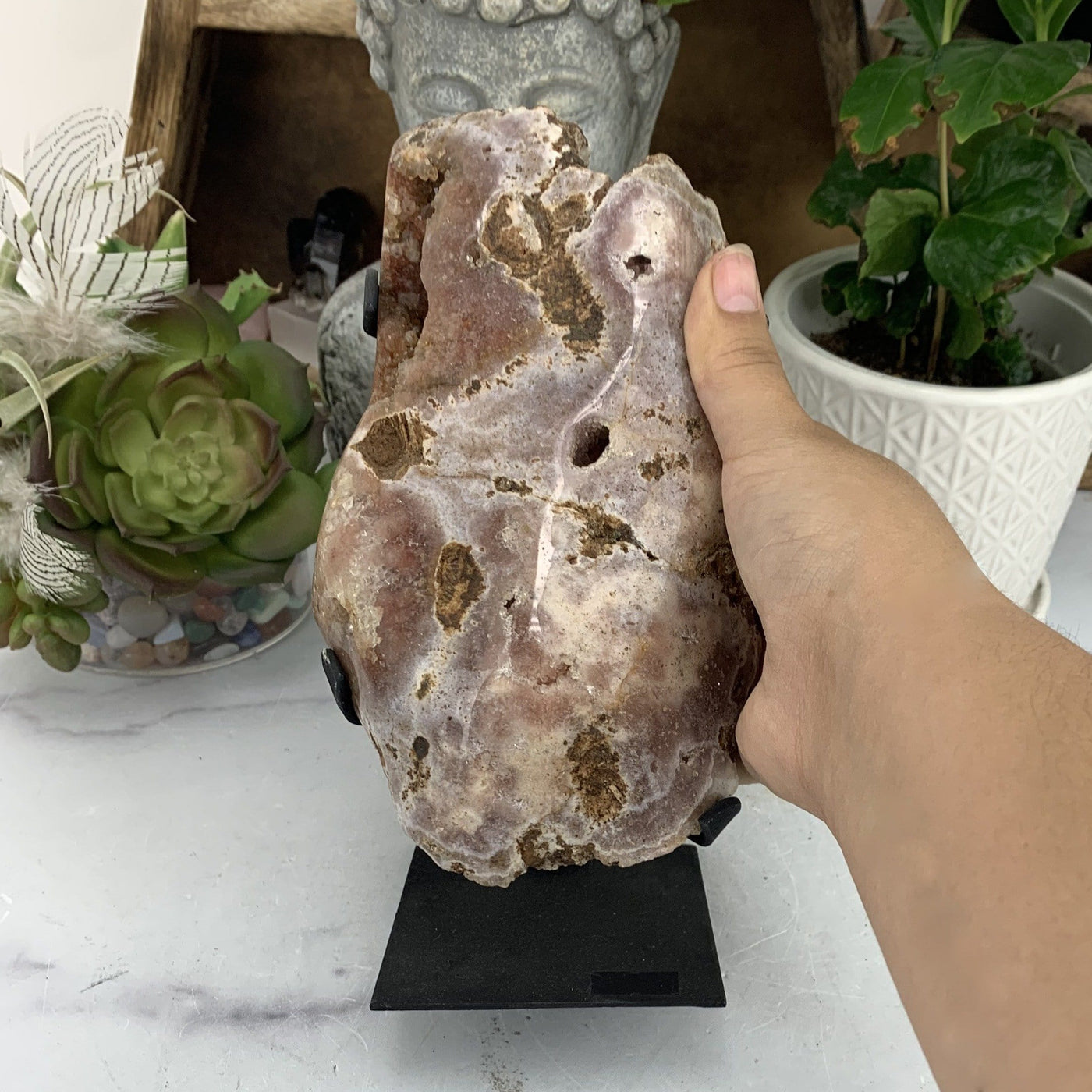 hand next to Pink Amethyst on Metal Stand with decorations in the background