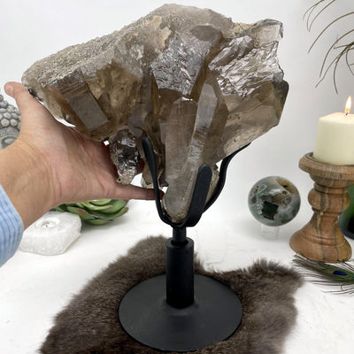 smokey quartz cluster on revolving metal base on display with hand for size reference