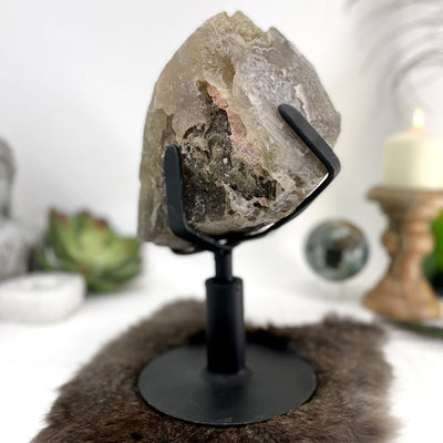 smokey quartz cluster on revolving metal base on display in front of backdrop