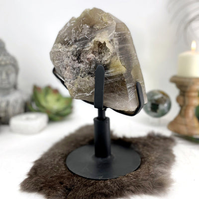 another view of smokey quartz cluster on reovlving metal base on display in front of backdrop