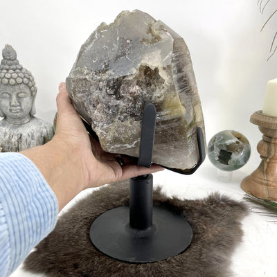 smokey quartz cluster on revolving metal base in front of backdrop with hand for size reference