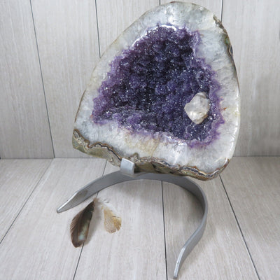 Large amethyst geode formation.  It has a white border with amethyst cluster purple inside and one calcite white formation on the right bottom side.  It is on a silver metal stand.